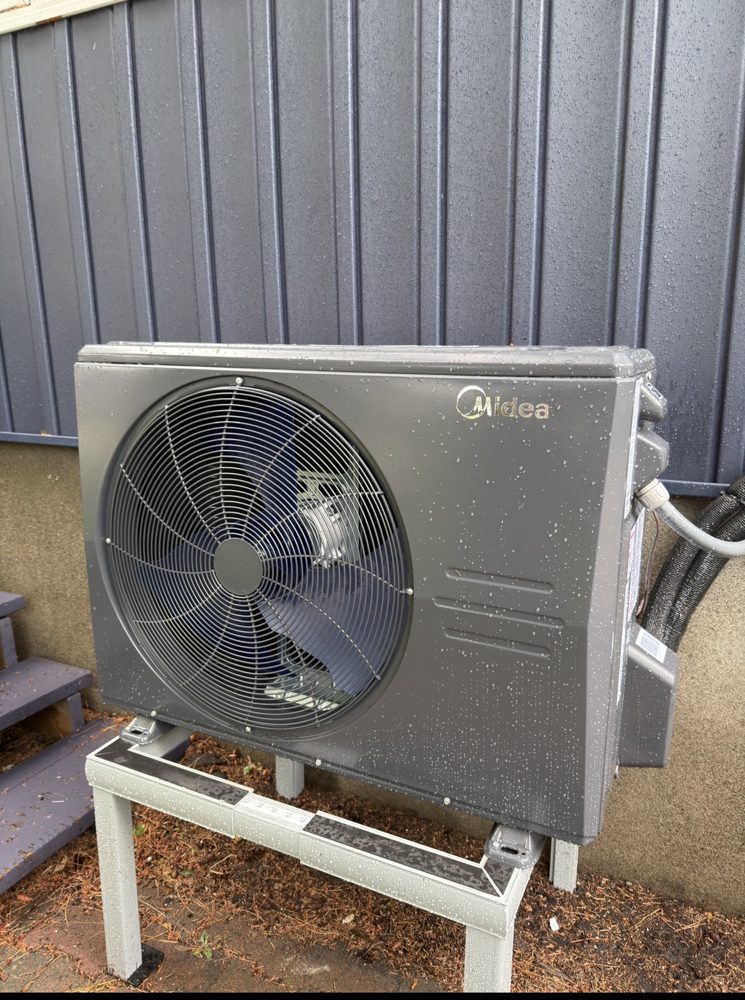 Grey heat pump outdoor unit on a raised metal stand against blue siding