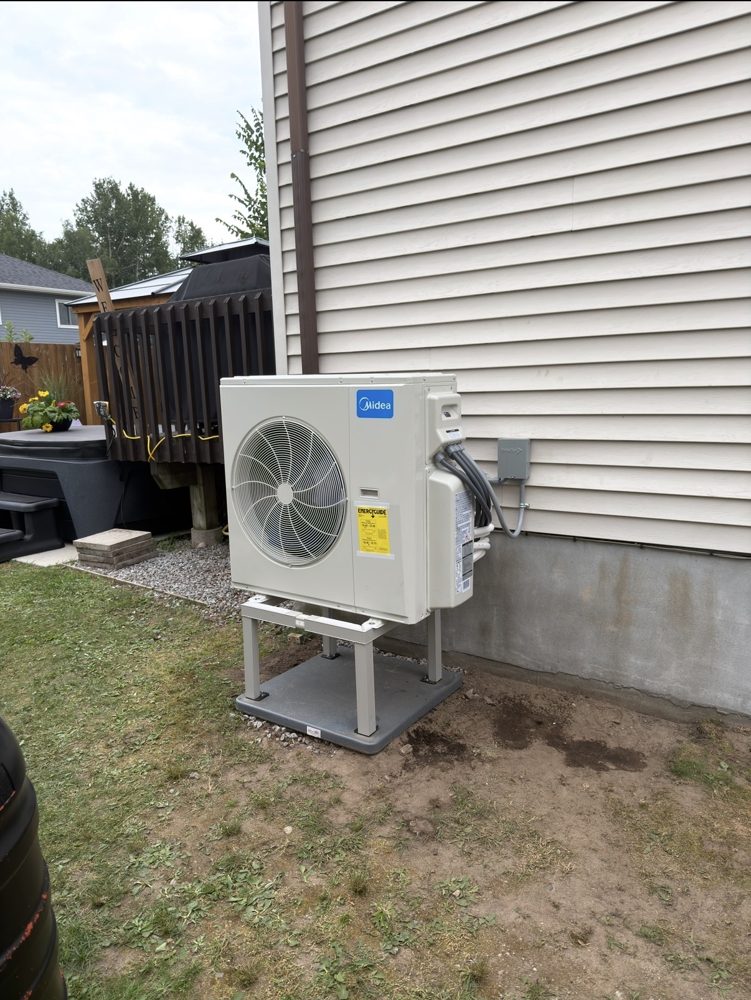 Multi-head ductless heat pump outdoor unit on a raised stand and pad beside a house